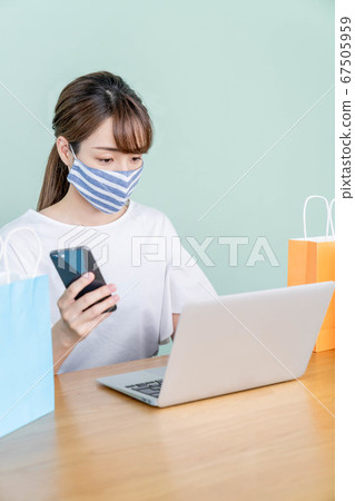 一個年輕的女子，與智能手機和一台電腦在線購物[戴著面具] 67505959