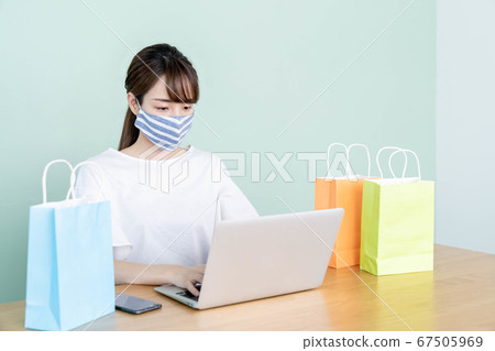 A young woman shopping online with a computer [wearing a mask] 67505969
