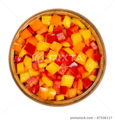 Diced bell peppers in a wooden bowl. Sweet pepper, capsicum or also called paprika, cut in colorful chips. Fresh yellow, orange and red fruits of Capsicum annuum. Closeup from above, macro food photo. 67506117