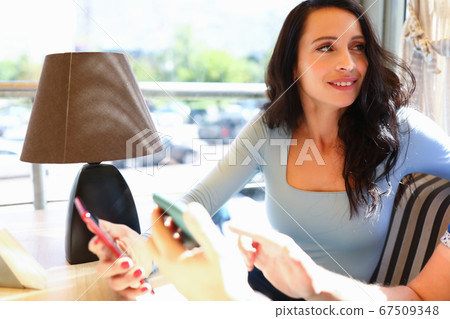 Woman sits in cafe with friend and holds smartphones in her hand Woman sits in cafe with friend and holds smartphones in her hand 67509348