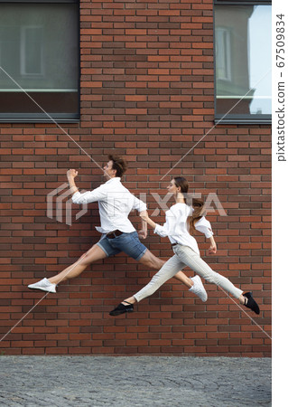 Jumping young couple in front of buildings, on the run in jump high 67509834