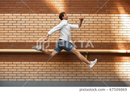 Jumping young man in front of buildings, on the run in jump high Jumping young man in front of buildings, on the run in jump high 67509869