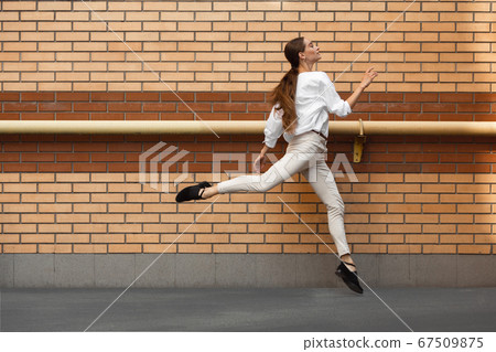Jumping young woman in front of buildings, on the run in jump high 67509875