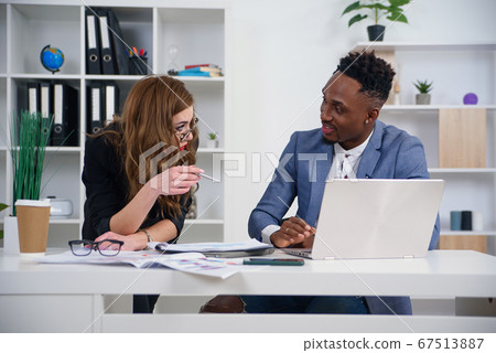Two diverse businesspeople chatting sitting behind laptop in office. Excited caucasian female sharing ideas or startup business plan with black male coworker. Informal conversation, work break concept 67513887