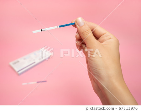 Female hand holding positive pregnancy test isolated on pink background. The abbreviation HCG on the blue bar means Human chorionic gonadotropin is a hormone produced by cells that are surrounding a 67513976