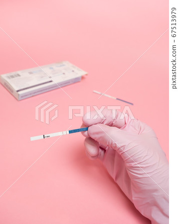Female hand in a pink medical glove holding positive pregnancy test isolated on pink background. The abbreviation HCG on the blue bar means Human chorionic gonadotropin is a hormone produced by cells Female hand in a pink medical glove holding positive pregnancy test isolated on pink background. The abbreviation HCG on the blue bar means Human chorionic gonadotropin is a hormone produced by cells 67513979