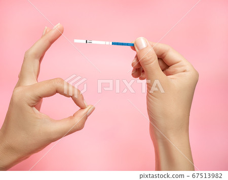 Female hand holding positive pregnancy test and Showing gesture OK isolated on pink background. The abbreviation HCG on the blue bar means Human chorionic gonadotropin is a hormone produced by cells 67513982