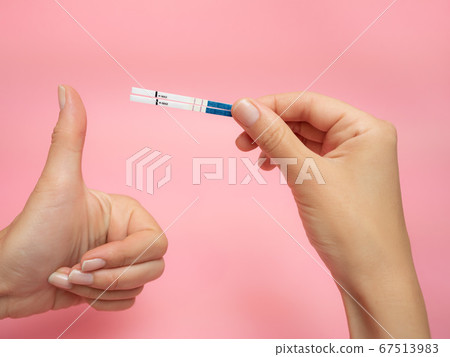 Female hand holding positive pregnancy test and Showing thumb up gesture isolated on pink background. The abbreviation HCG on the blue bar means Human chorionic gonadotropin is a hormone produced by Female hand holding positive pregnancy test and Showing thumb up gesture isolated on pink background. The abbreviation HCG on the blue bar means Human chorionic gonadotropin is a hormone produced by 67513983