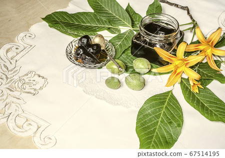 Glass jar with nut jam near the green walnuts with leaves and orange lilies Glass jar with nut jam near the green walnuts with leaves and orange lilies 67514195