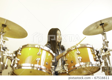 A cute Asian elementary school girl learning to play a drum in a classroom.  67516611