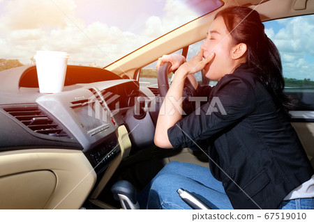 Young woman yawning while driving to work in the 67519010