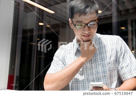 Handsome asian boy smiling and checking his smartphone in the hallway.  67519847