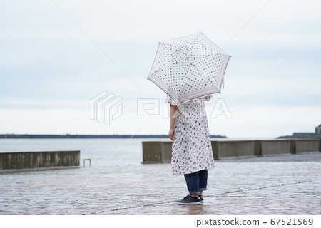 A woman standing by the seaside in the rain 67521569