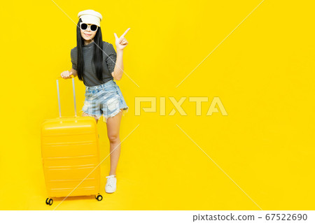 Young Asian female tourist in casual clothes and sunglasses Carrying a  passport to go to travel sitting on a luggage isolated on yellow background copy space,Vacation,holidays and travel concept 67522690