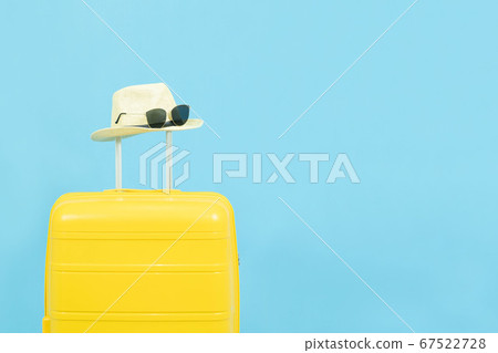 Summer holidays, vacation and travel concept.Yellow Suitcase or luggage bag and the fashion sunglasses on hat isolated on blue background with copy space 67522728