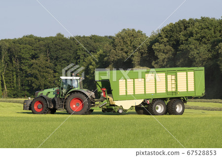 Green tractor picking up cut grass Green tractor picking up cut grass 67528853