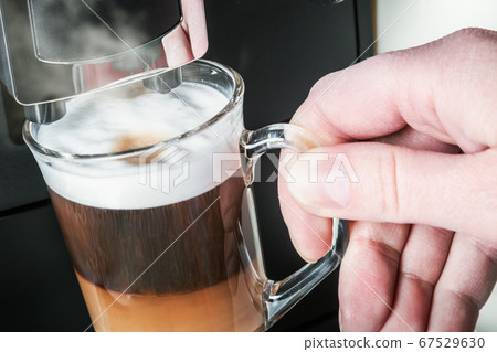 hand picks up a glass of hot cappuccino with foam made hand picks up a glass of hot cappuccino with foam made 67529630