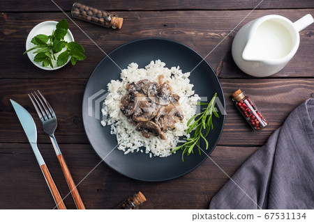 Risotto with mushrooms on a black plate. Boiled white rice with champignons in cream sauce. Dark wooden background. 67531134