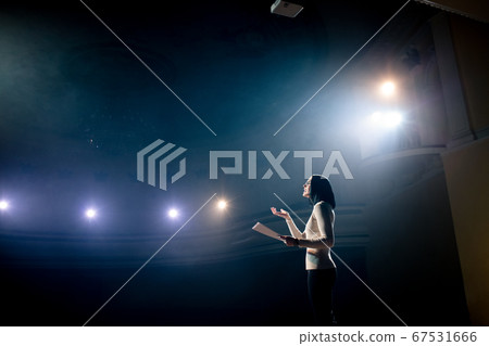 Expert perform on the stage address to modern crowd audience sitting and listening in large hall. Female entrepreneur communicating with a listener at workshop convention for young businesspersons 67531666