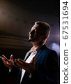 Showman. Middle Age Male entertainer, presenter or actor on stage. Arms to sides, smoke on background of spotlight. Front view portrait of a male public speaker speaking at the microphone, pointing 67531694