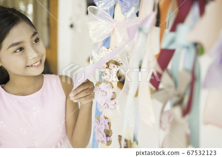 A cute Asian schoolgirl is enjoying buying a hair bow at the store. 67532123