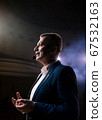 Showman. Middle Age Male entertainer, presenter or actor on stage. Arms to sides, smoke on background of spotlight. Front view portrait of a male public speaker speaking at the microphone, pointing 67532163