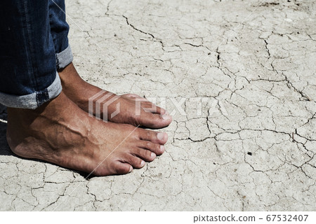 bare feet of a man on a cracked dry soil 67532407