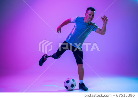 Athlete with disabilities or amputee isolated on gradient studio background. Professional male football player with leg prosthesis training and practicing in studio. Athlete with disabilities or amputee isolated on gradient studio background. Professional male football player with leg prosthesis training and practicing in studio. 67533390