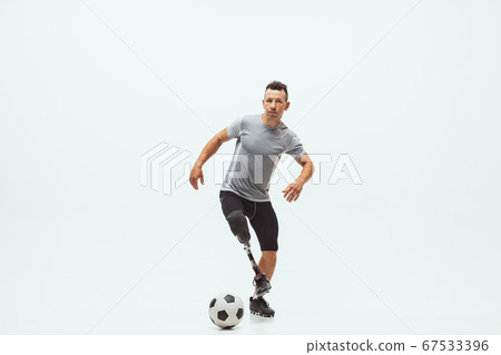 Athlete with disabilities or amputee isolated on white studio background. Professional male football player with leg prosthesis training and practicing in studio. Athlete with disabilities or amputee isolated on white studio background. Professional male football player with leg prosthesis training and practicing in studio. 67533396