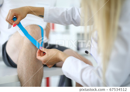 Nurse fastens kinesio tape on her leg 67534512