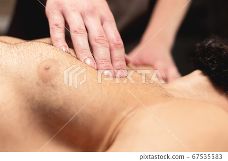 A professional therapist massages the pectoral muscle of an athlete to a man in a professional massage salon. The concept of professional help of a manal therapist 67535583