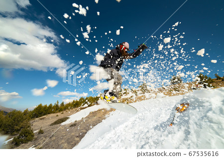 Stylish young girl snowboarder does the trick in jumping from a snow kicker against the blue sky clouds and mountains in the spring. Stylish young girl snowboarder does the trick in jumping from a snow kicker against the blue sky clouds and mountains in the spring. 67535616