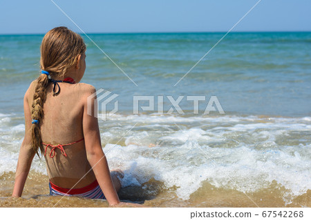 A girl sits on a sandy sea beach and looks into A girl sits on a sandy sea beach and looks into 67542268