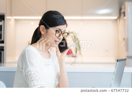 在家工作一名戴著眼鏡的女人在餐廳的筆記本電腦前戴著智能手機 在家工作一名戴著眼鏡的女人在餐廳的筆記本電腦前戴著智能手機 67547732