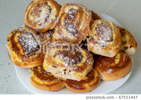 Patties with cottage cheese and raisins piled up on a white plate. Pies sprinkled with powdered sugar Patties with cottage cheese and raisins piled up on a white plate. Pies sprinkled with powdered sugar 67551447
