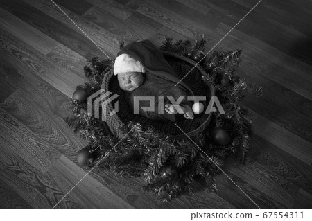 a newborn baby sleeps in a red cap with a pompom in a Christmas wreath 67554311