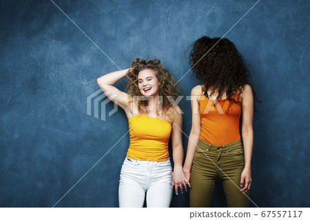 young pretty teenage girls friends with blond and brunette curly hair posing cheerful on blue background, lifestyle people concept young pretty teenage girls friends with blond and brunette curly hair posing cheerful on blue background, lifestyle people concept 67557117