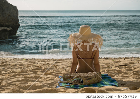 Beautiful tan young woman laying on the beach sunbathing at the seaside wearing big straw hat 67557419