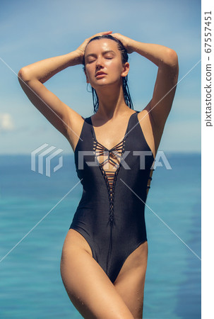 Young beautiful woman in black bikini swimsuit over ocean background during hot sunny summer day. Tropical vacation Young beautiful woman in black bikini swimsuit over ocean background during hot sunny summer day. Tropical vacation 67557451