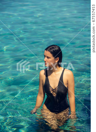Young beautiful woman in black bikini in the pool during hot sunny summer day. Tropical vacation 67557453