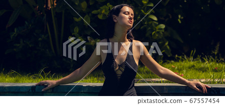 Young beautiful woman in black bikini in the pool during hot sunny summer day. Tropical vacation 67557454