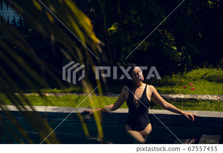 Young beautiful woman in black bikini in the pool during hot sunny summer day. Tropical vacation 67557455