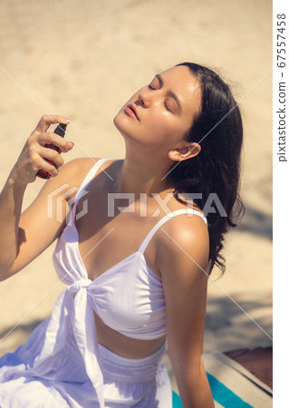 Young beautiful woman spraying thermal water or facial mist on her face at the beach. Summer skin care Young beautiful woman spraying thermal water or facial mist on her face at the beach. Summer skin care 67557458