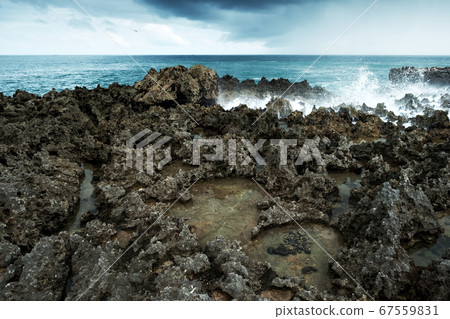 Waves break on rocky shore. 67559831