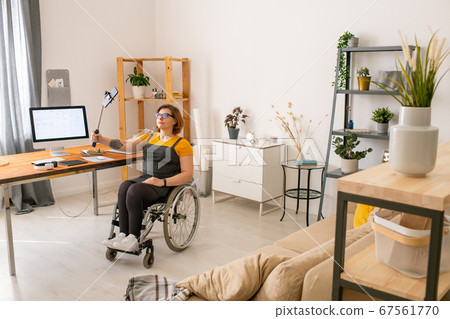 Young disable female blogger in wheelchair holding stick with smartphone 67561770