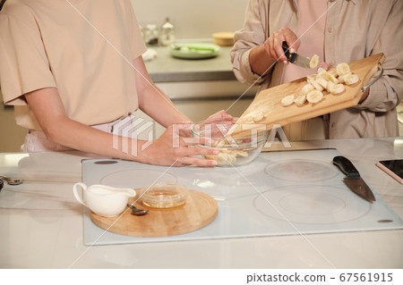 Young female putting banana slices into glass bowl during cooking masterclass 67561915