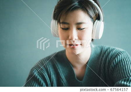 Woman in her 30s listening to music with wireless headphones Woman in her 30s listening to music with wireless headphones 67564157