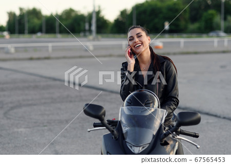 Portrait of a serious biker waiting during a phone call to insurance on a motorbike on the street 67565453