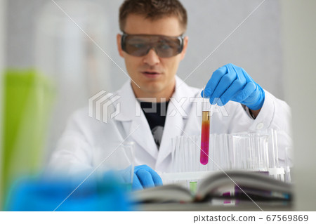 A male chemist holds test tube of glass in his hand overflows a liquid solution A male chemist holds test tube of glass in his hand overflows a liquid solution 67569869