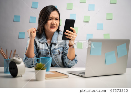 Asian woman angry looking at smart phone reading Asian woman angry looking at smart phone reading 67573230
